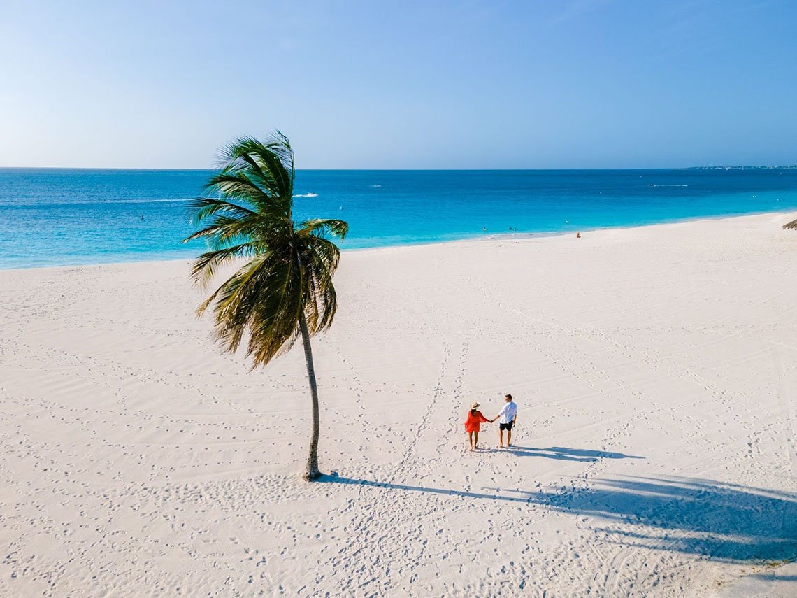 An aerial shot of a couple walking on Eagle Beach's shoreline in Aruba.