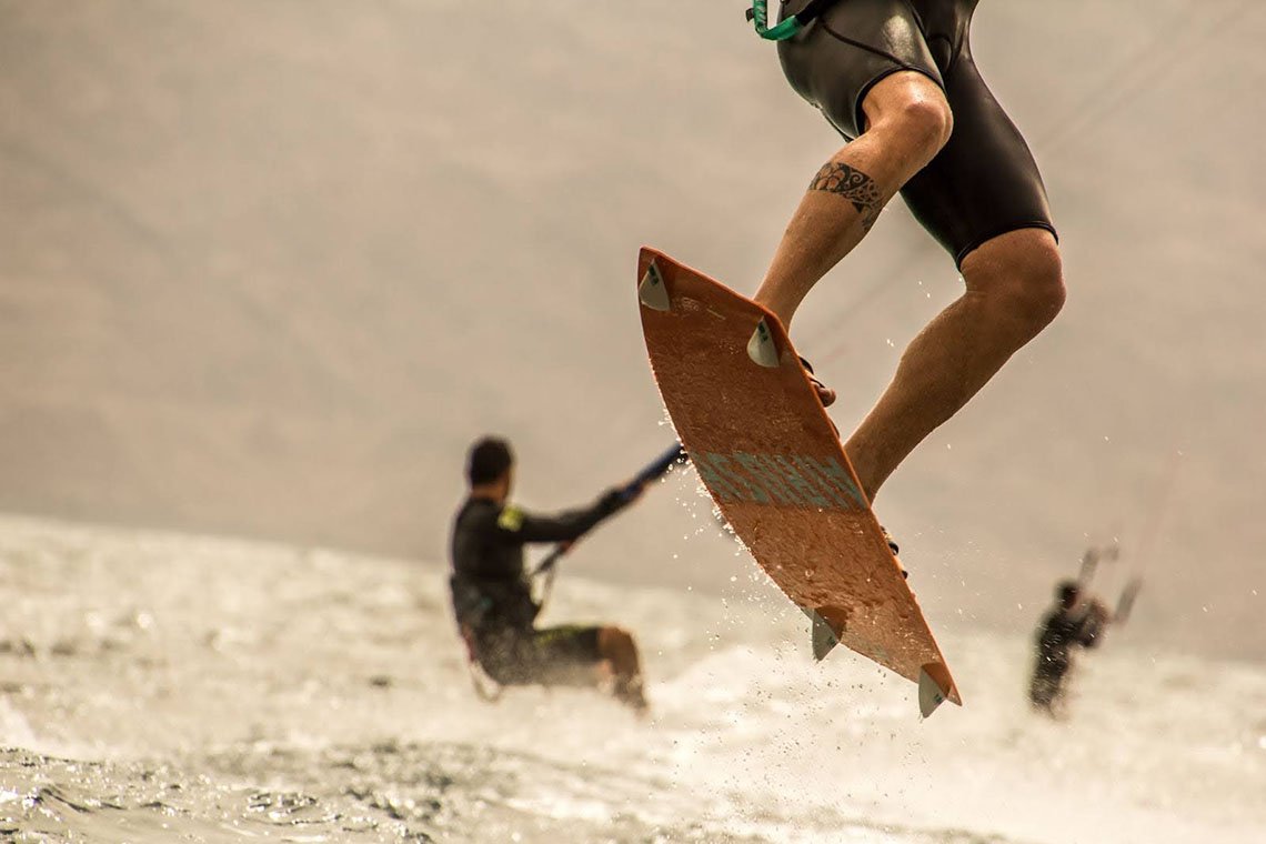 A half-body shot of a man wakeboarding across Aruba's clear waters, with two other riders visible in the distance