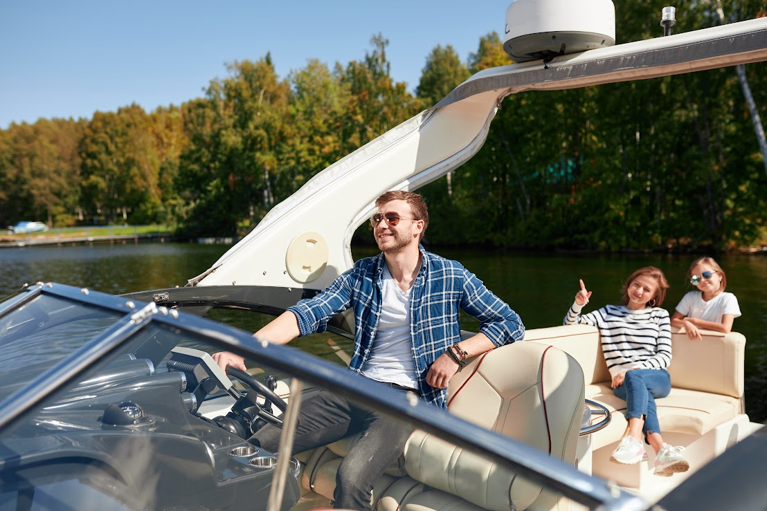 A family is relaxing on the boat while the dad steers the boat.