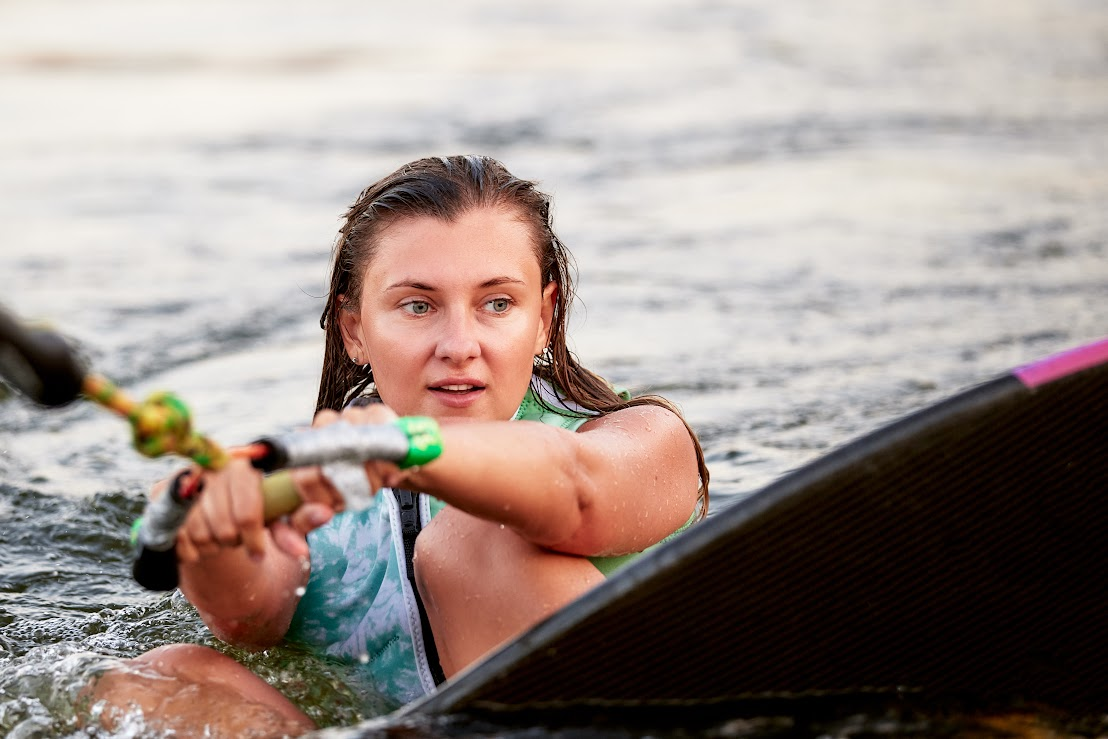 A young woman is kneeboarding in the water and grabbing onto a handle.