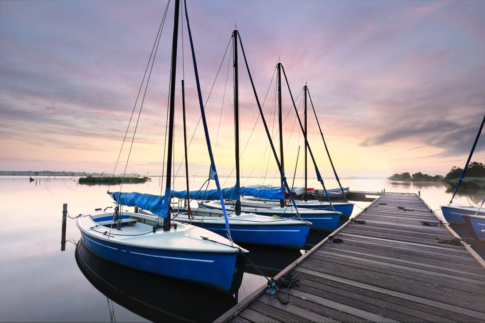 Sail boats tied to a small dock in the ocean at dawn.