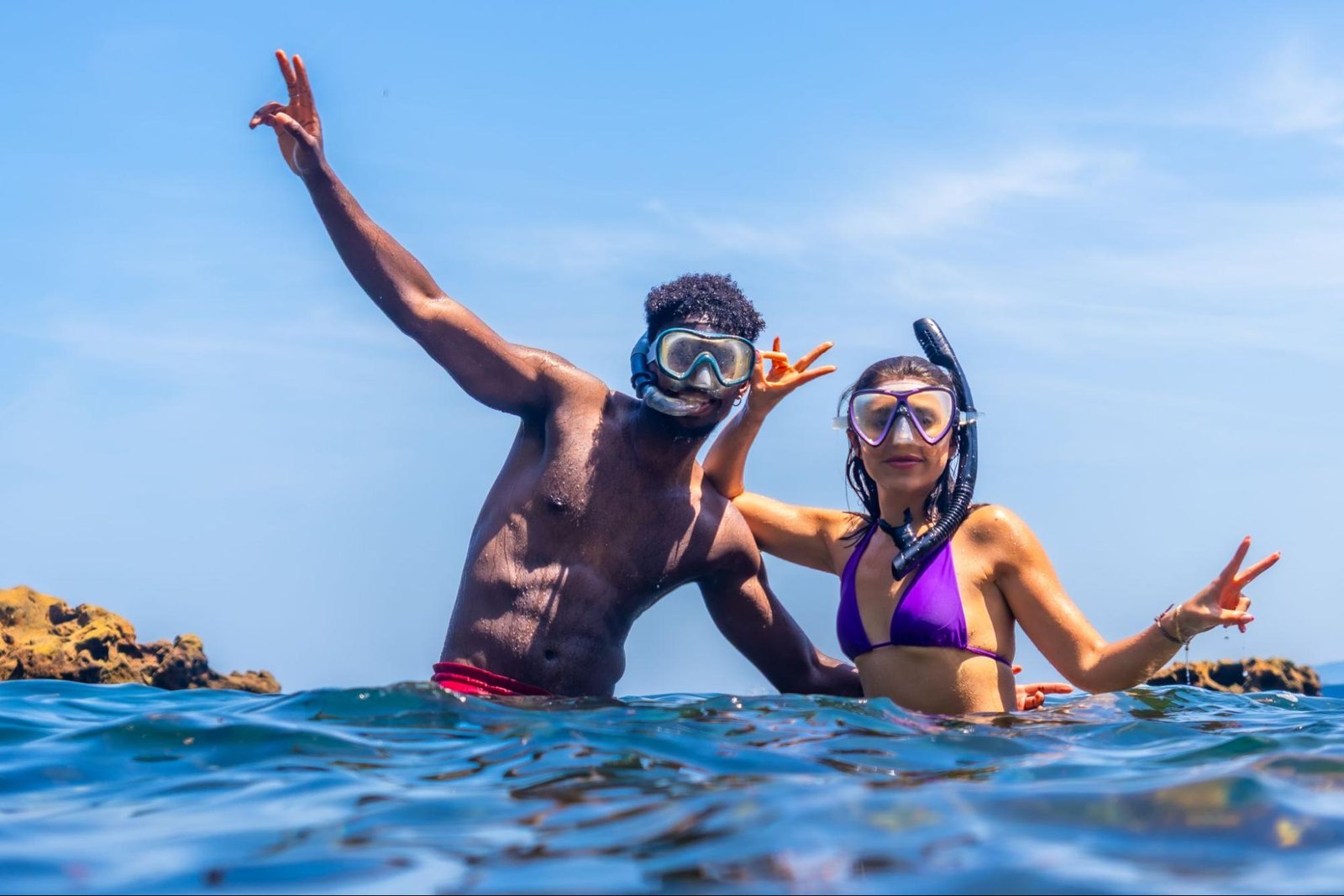 A man and a woman in the ocean wearing bathing suits and snorkeling gear.