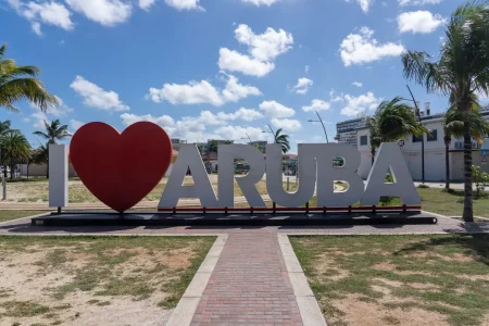 An image of a large "I Love Aruba" sign, set against a sunny sky and palm trees.